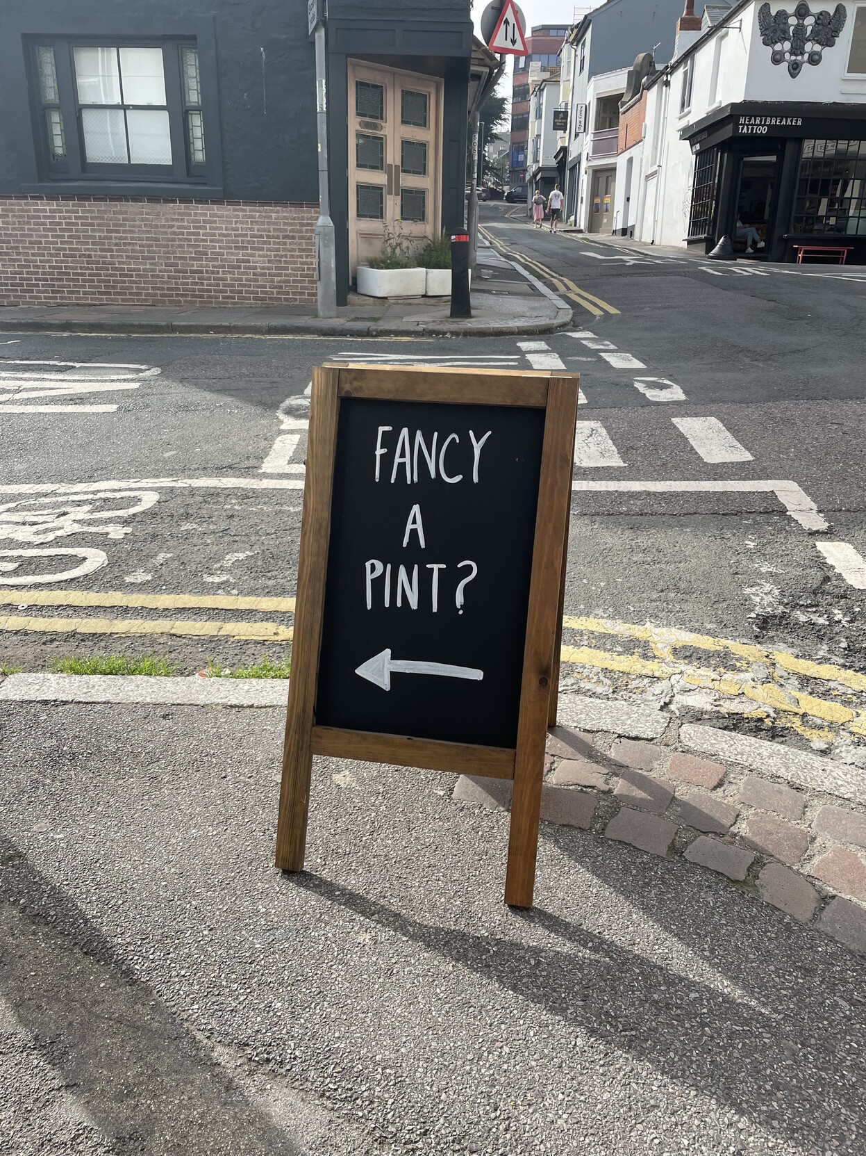 On a street corner, a sign saying “fancy a pint?” with an arrow pointing to the street on the left.