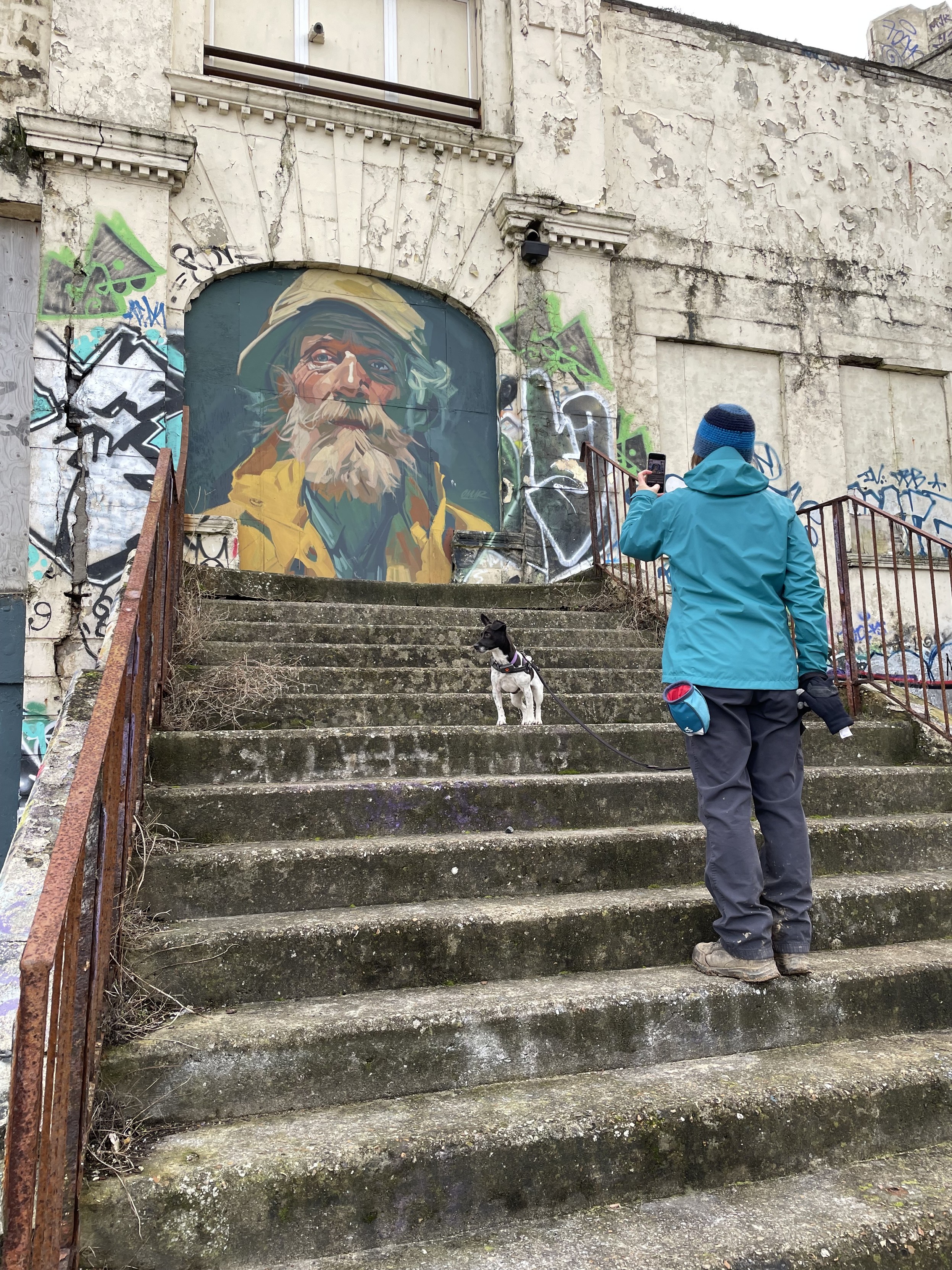 A most lovely human takes a photo of street art at Margate’s Lido. A small mixed breed terrier, who is a very good girl, sits on the steps.