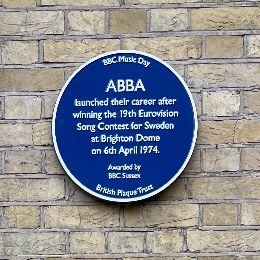 A blue circular sign on a wall of the Brighton Dome Concert Hall reading: “ABBA launched their career after winning the 19th Eurovision Song Contest for Sweden at Brighton Dome on 6th April 1974”